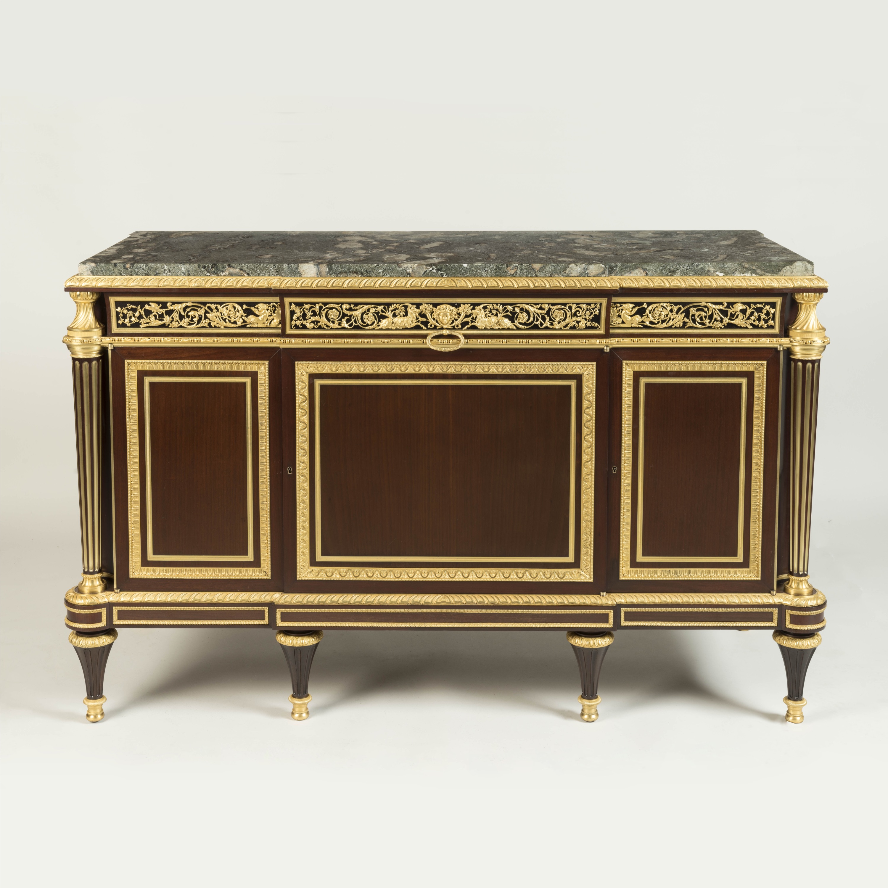 An ornate French Louis XVI style mahogany commode (credenza) featuring a dark green marble top, rich gilt-bronze (ormolu) mounts, and detailed paneling, set against a plain off-white background.