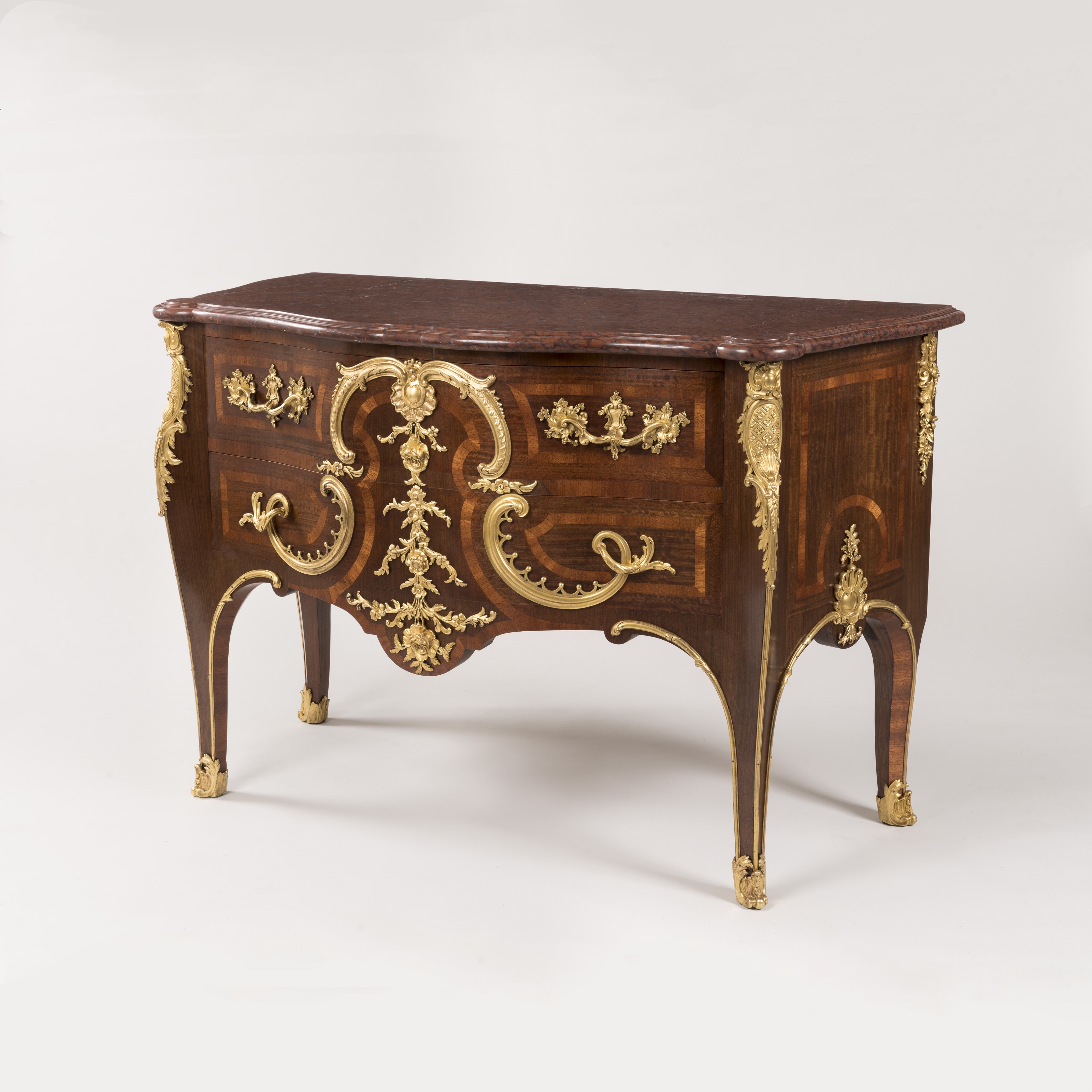 A wooden commode with intricate gold accents, set against a plain background, showcasing luxurious design in a minimalist setting.